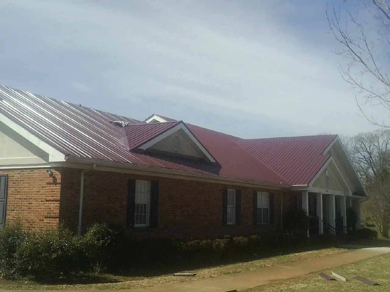 Red metal roof with gabled entries on a long brick building, from a Hail Damage Roof Repair job in Watertown